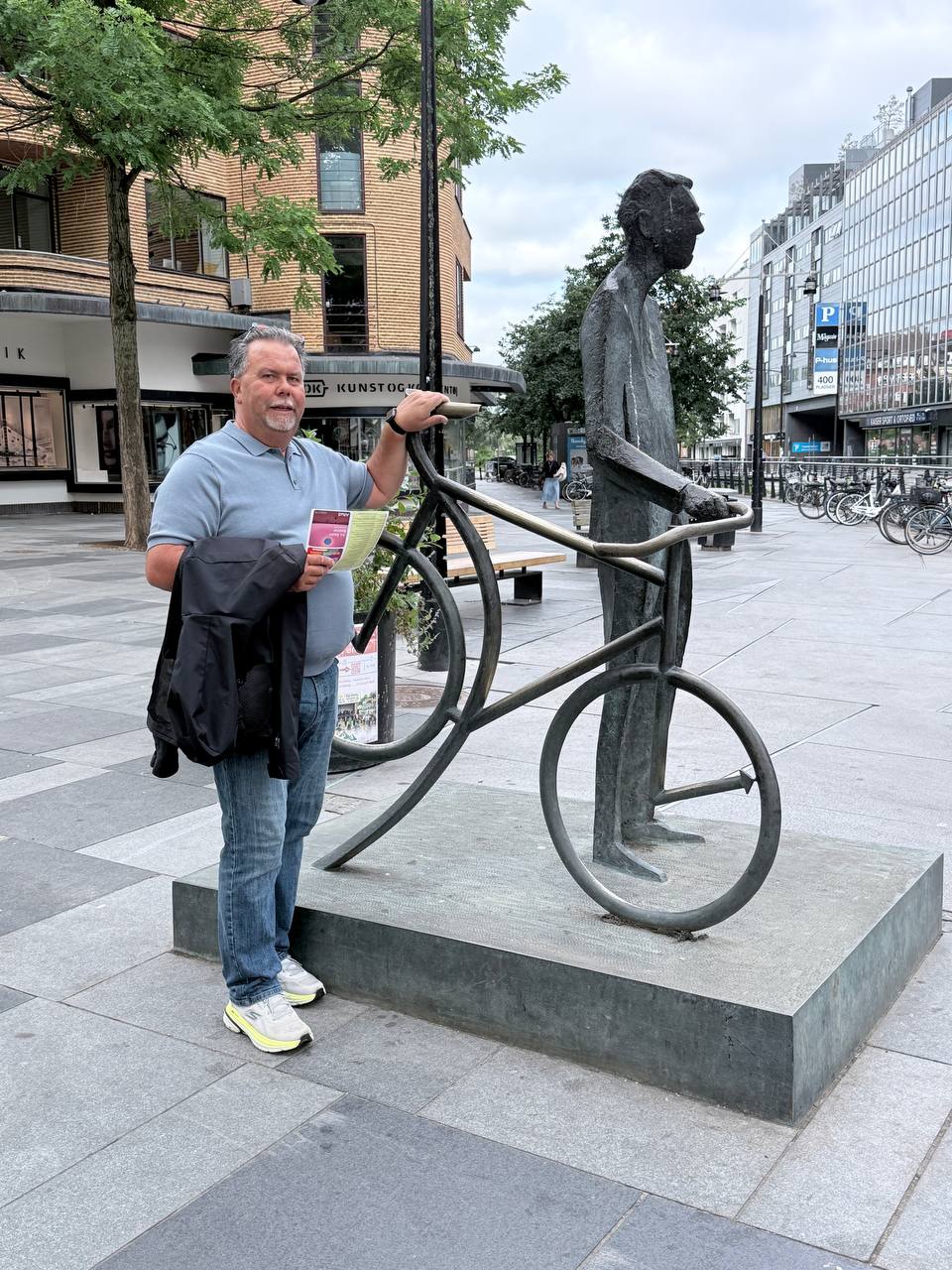 Man posing next to a dark metal bicycle sculpture outside Kunsthal in Aarhus