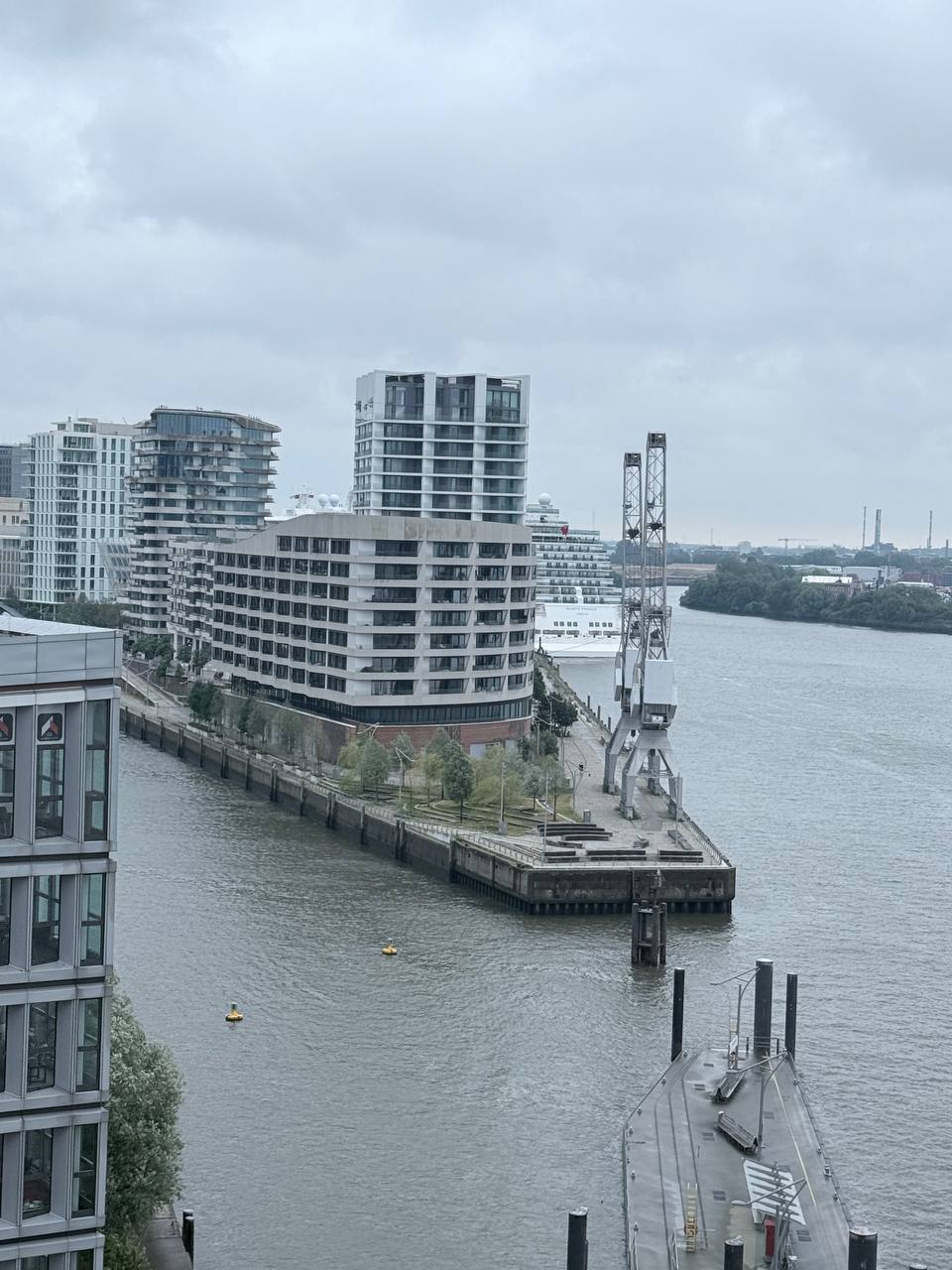 Modern waterfront with crane, cruise ship and residential towers on grey day