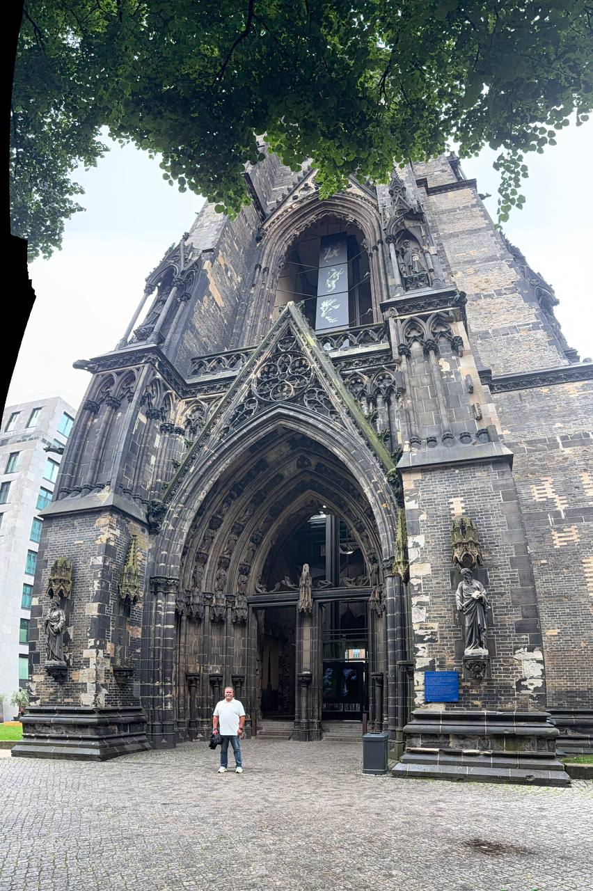 Grand Gothic church facade with statues, ornate stonework and a person for scale on cobblestones