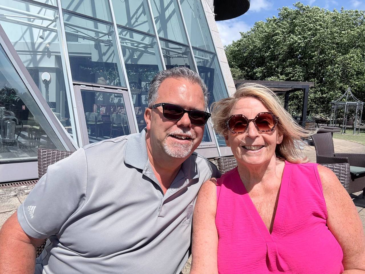 Angie and Iain smiling in sunglasses on a sunny patio