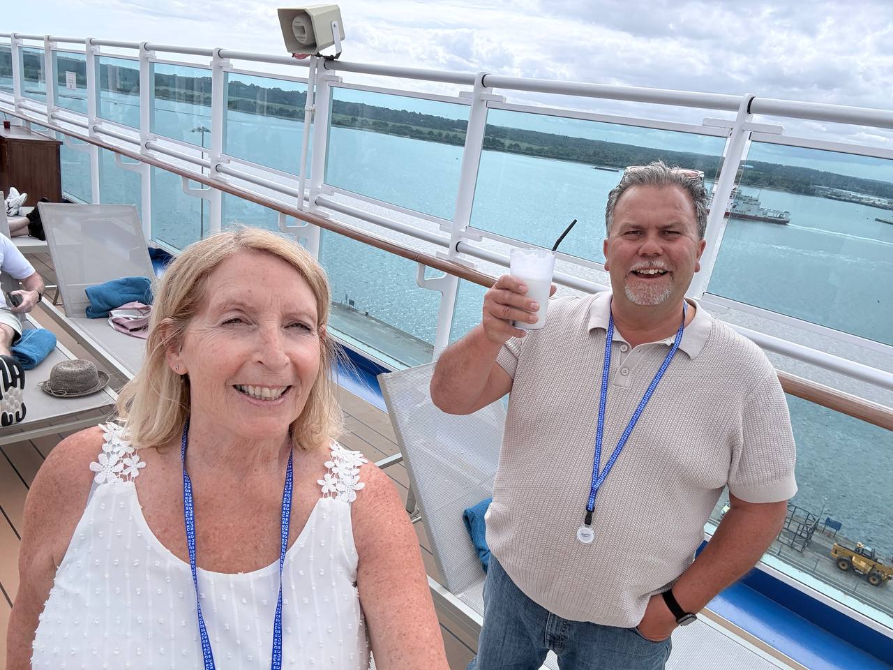 Two couples on cruise ship deck during sail away party - raising glasses, smiling, city and water background