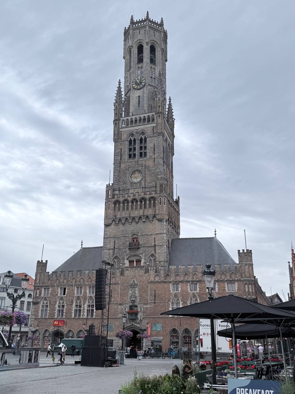 The 83-metre Belfry of Bruges rising above the Grote Markt, with Gothic windows, clock faces, and a sky of fluffy white clouds