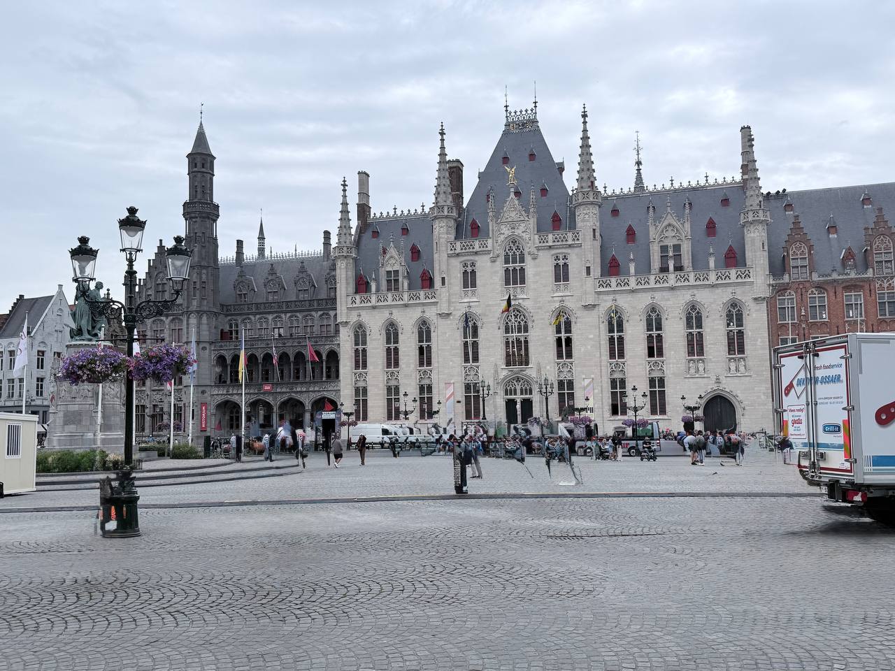Wide view of the Grote Markt in Bruges with the iconic bell tower, Gothic and Renaissance buildings, cobblestone square, and outdoor cafés