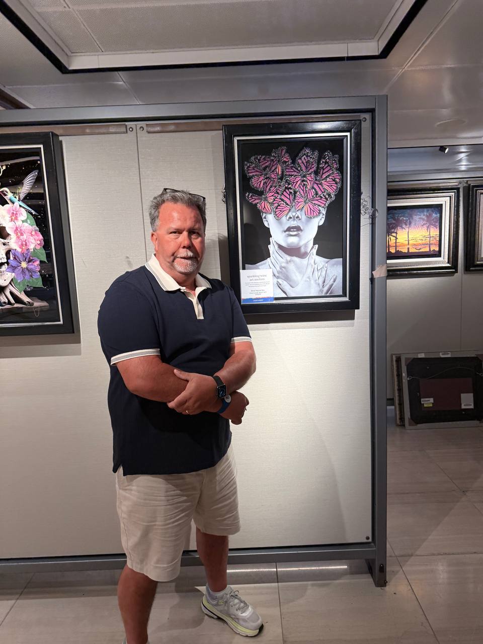 Man in navy polo standing in an art gallery with butterfly artwork