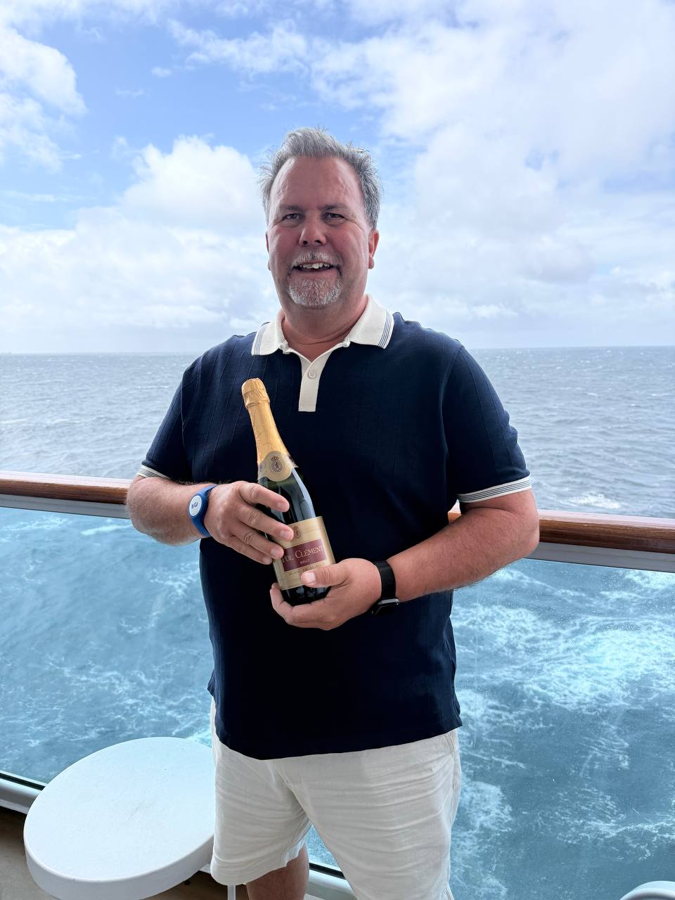 Man holding champagne bottle on ship deck with ocean background