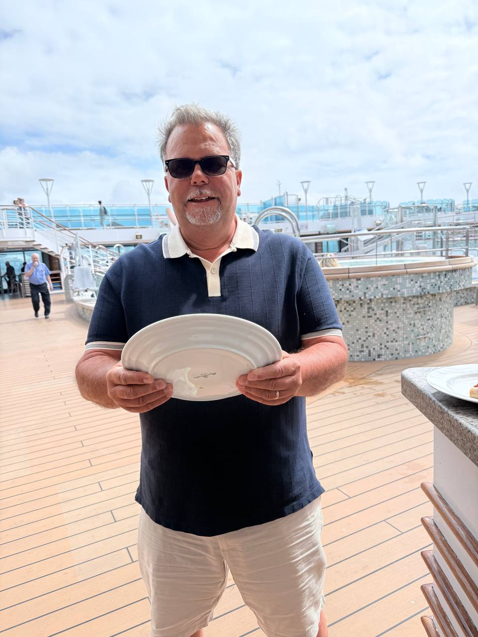 Man holding a large white plate on ship deck, pretending to steer the ship