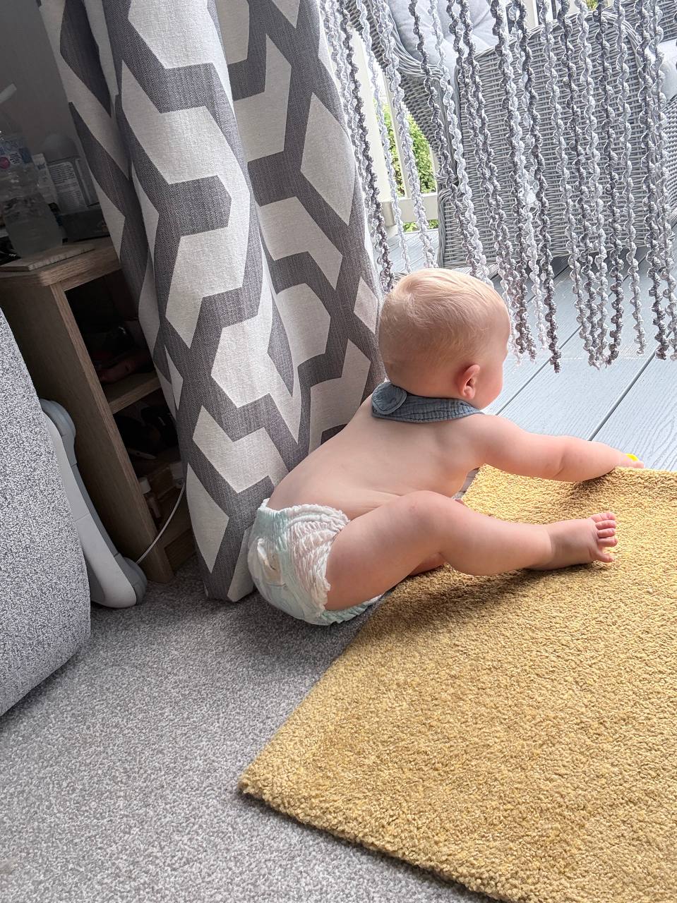 Theo sitting on the yellow rug looking out through the glass door at the garden
