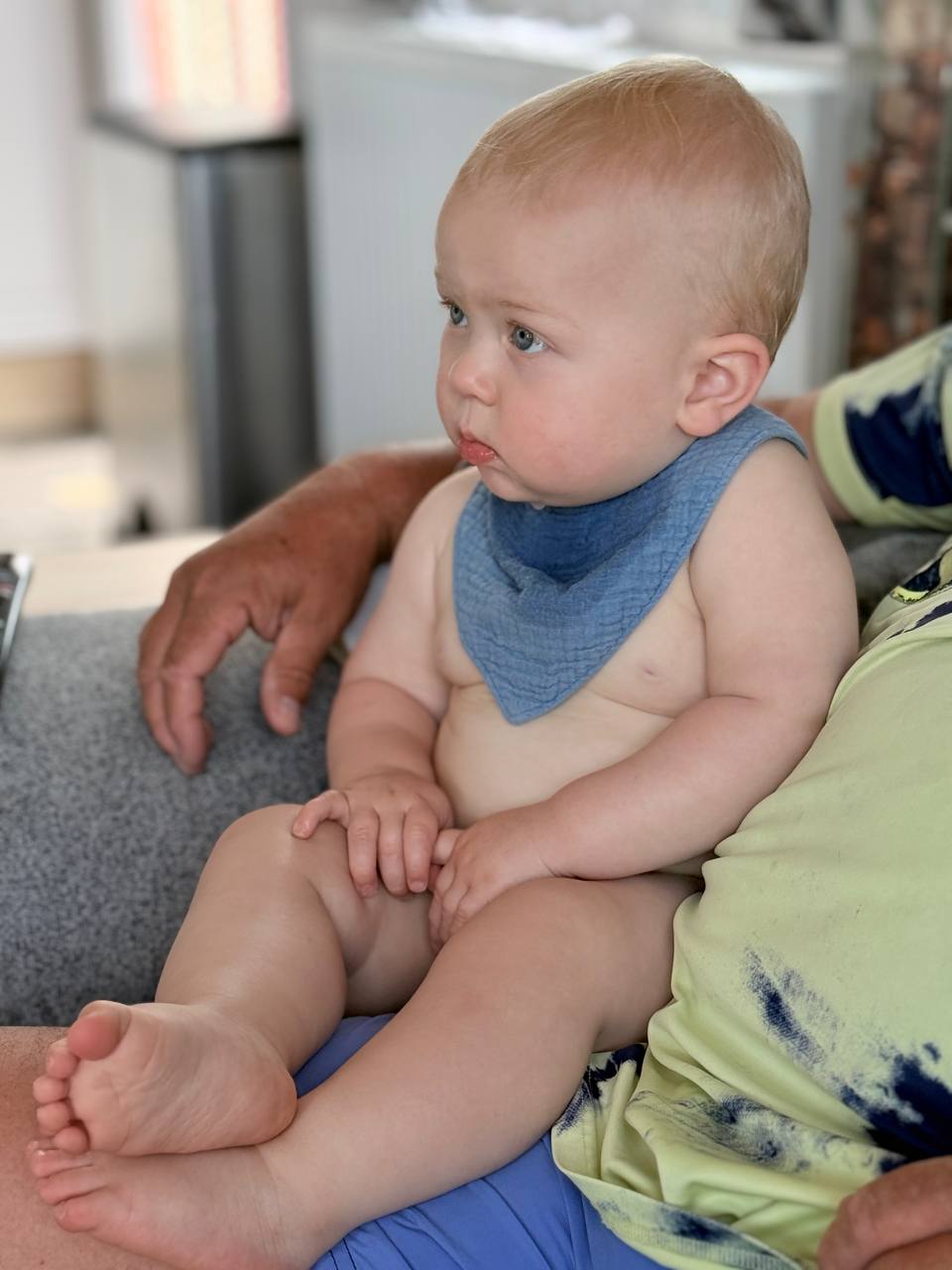 Theo sitting on Iain's lap on the gray couch, looking thoughtfully to the side