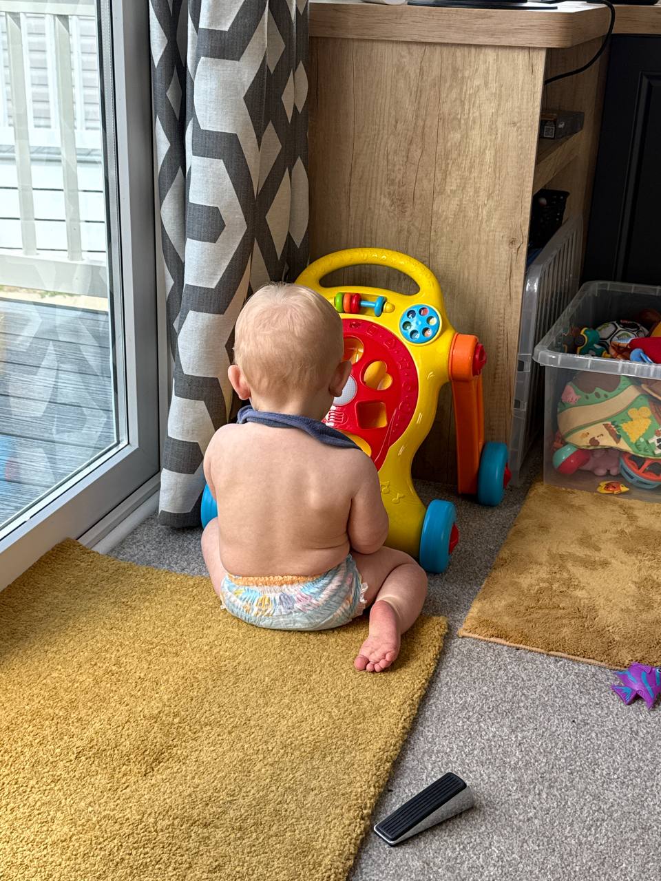 Theo sitting on the mustard-yellow rug, playing with his activity walker