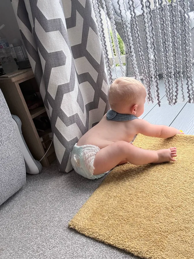 Theo sitting on the yellow rug looking out through the glass door at the garden