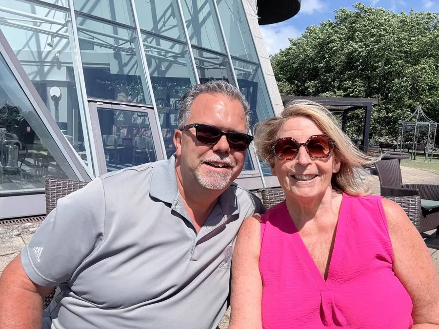 Angie and Iain smiling in sunglasses on a sunny patio