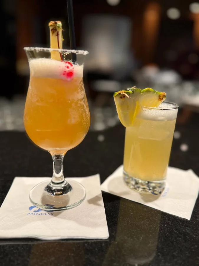Two cocktails on Princess branded napkins - tropical cocktail with pineapple garnish and short glass with pineapple wedge