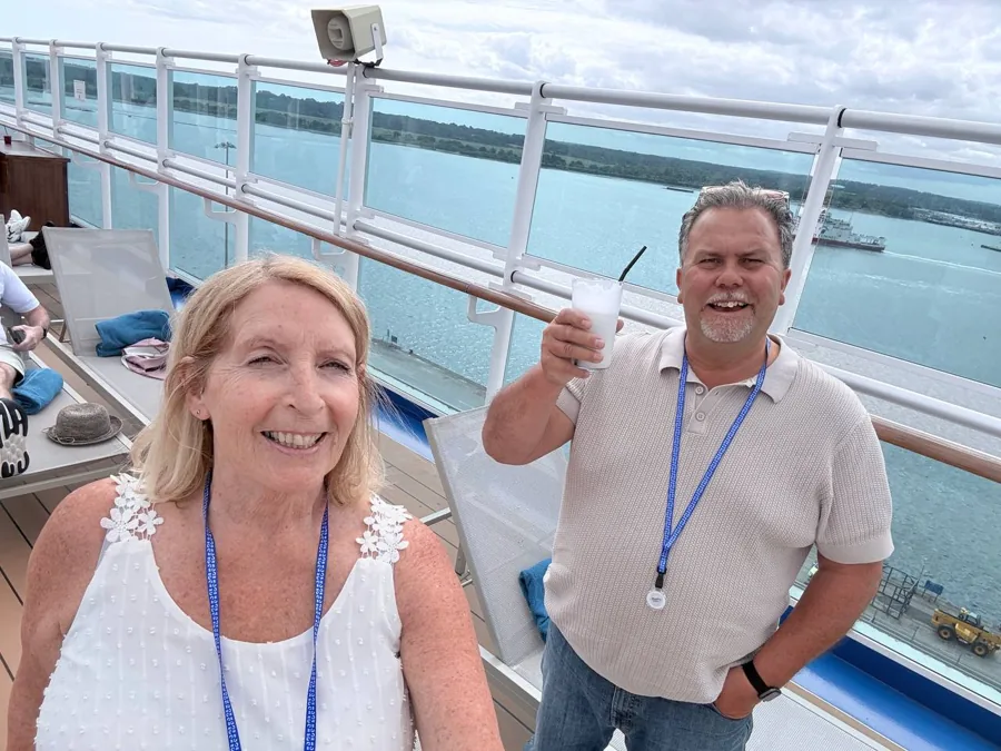 Two couples on cruise ship deck during sail away party - raising glasses, smiling, city and water background