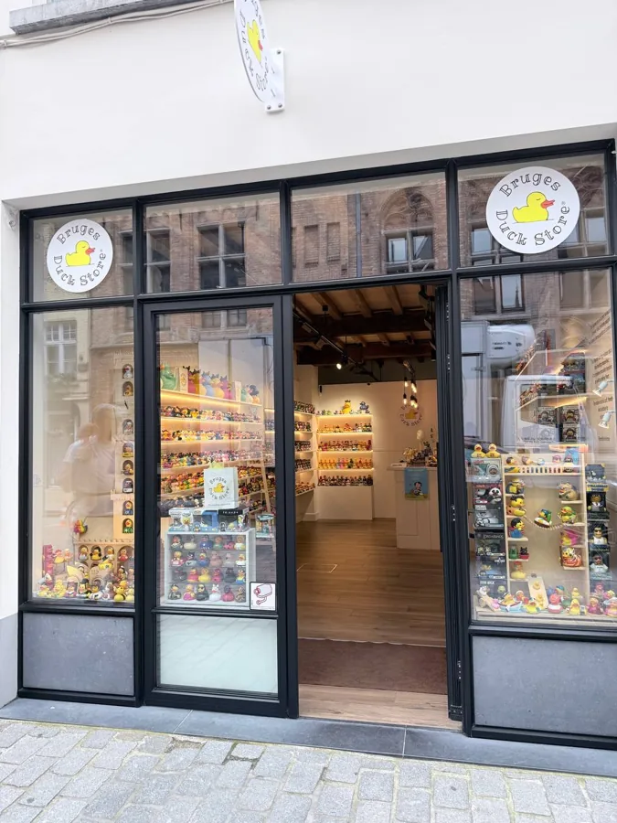 Bruges Duck Store with yellow rubber ducks visible through open glass doors, black-framed facade with white sign