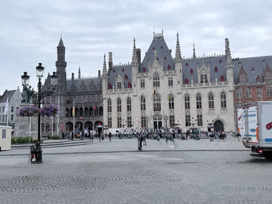 Wide view of the Grote Markt in Bruges with the iconic bell tower, Gothic and Renaissance buildings, cobblestone square, and outdoor cafés
