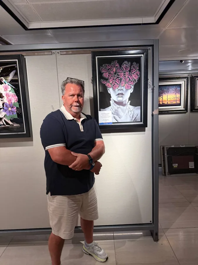 Man in navy polo standing in an art gallery with butterfly artwork