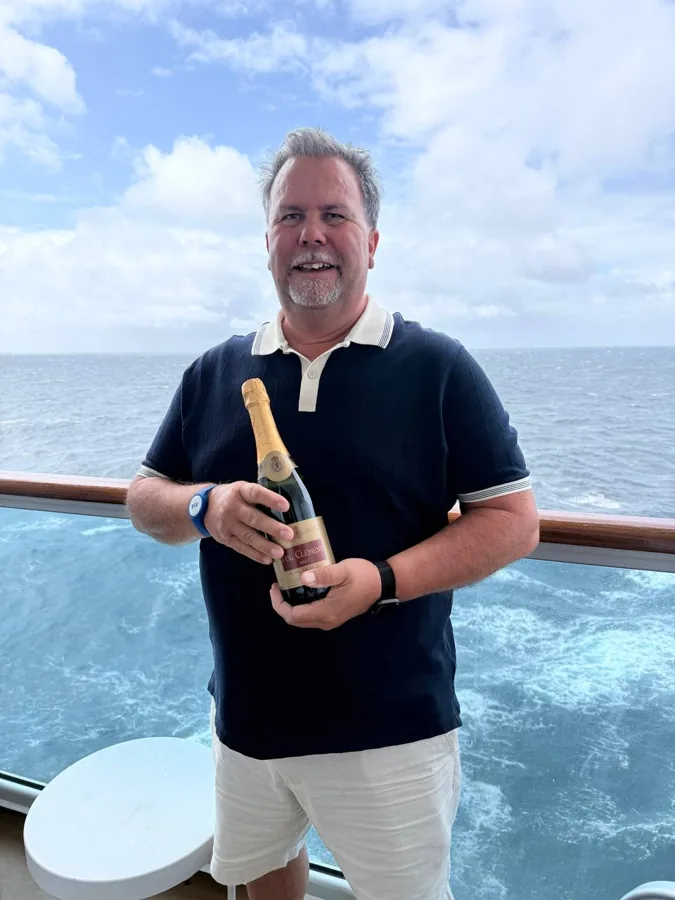 Man holding champagne bottle on ship deck with ocean background