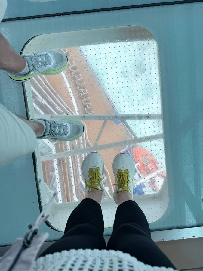 Looking down through glass floor walkway at feet and ground below