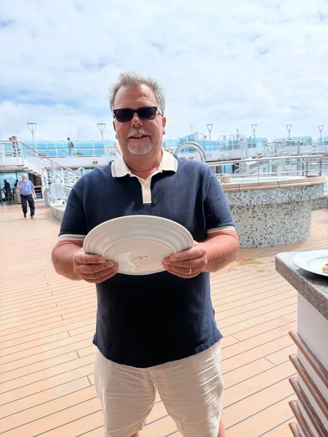 Man holding a large white plate on ship deck, pretending to steer the ship