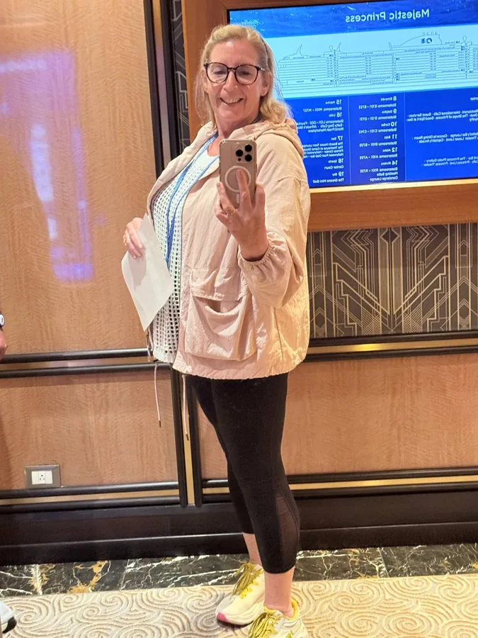 Woman in pink jacket doing mirror selfie with Majestic Princess deck plan