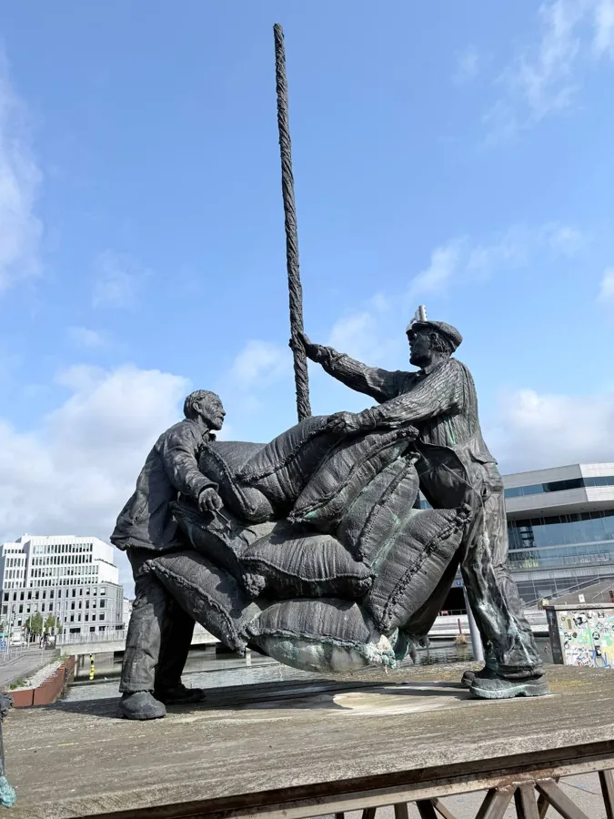 Bronze sculpture of two men loading sacks, Aarhus waterfront, blue sky