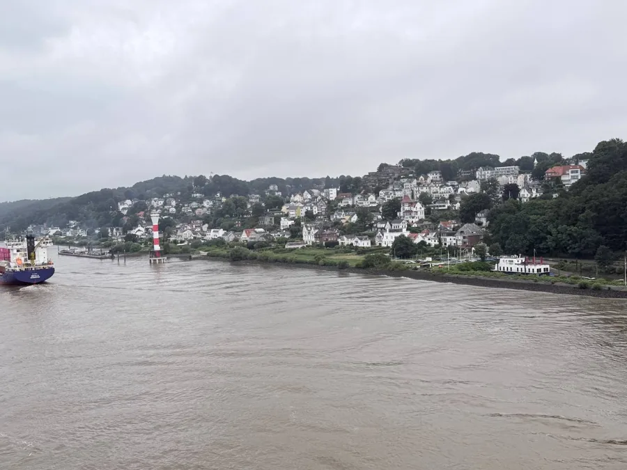 River scene with cargo ship, lighthouse and hillside town on an overcast day