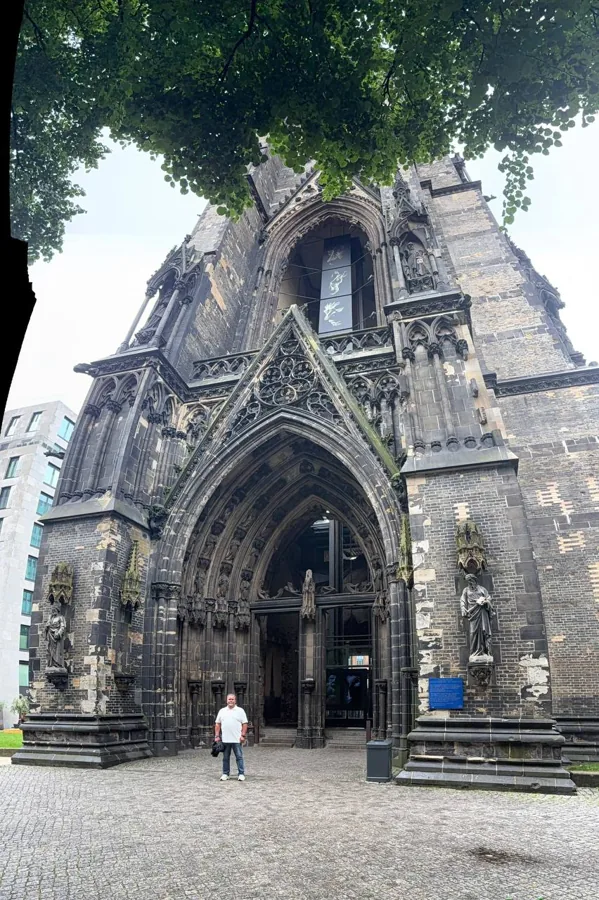 Grand Gothic church facade with statues, ornate stonework and a person for scale on cobblestones